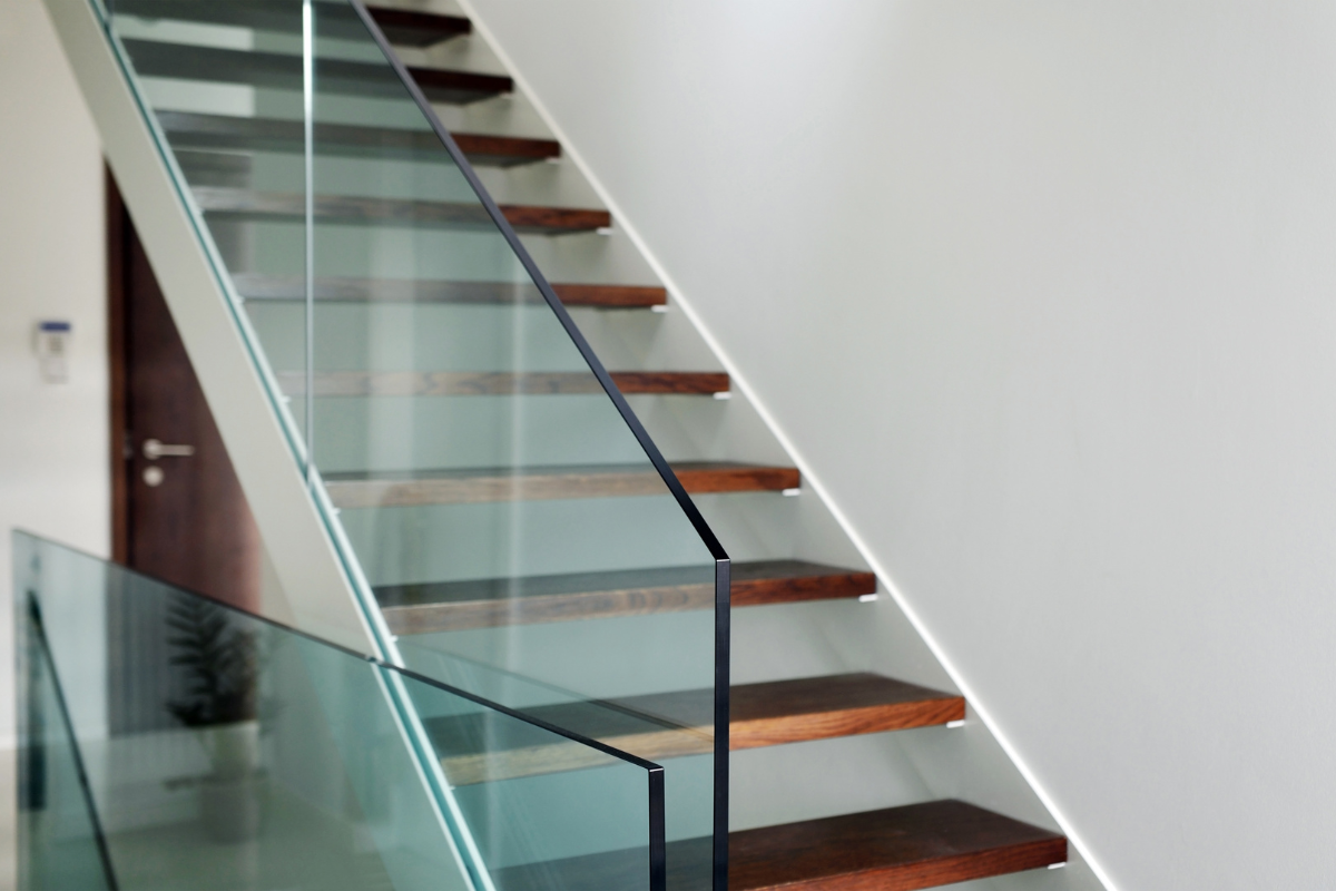 Barandilla de cristal. Escalera y pared blancas y es calones de madera
